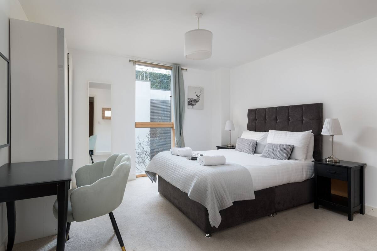 A modern bedroom with a large bed, bedside tables, a desk, and a chair.