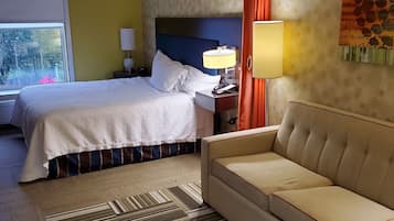 A hotel room with a bed, a sofa, a nightstand, a lamp, and a window with curtains.