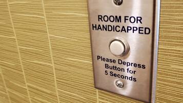 Ein metallisches Schild an einer strukturierten Wand, das ein Zimmer für Menschen mit Behinderung anzeigt, mit einer vertieften Taste für 5 Sekunden.