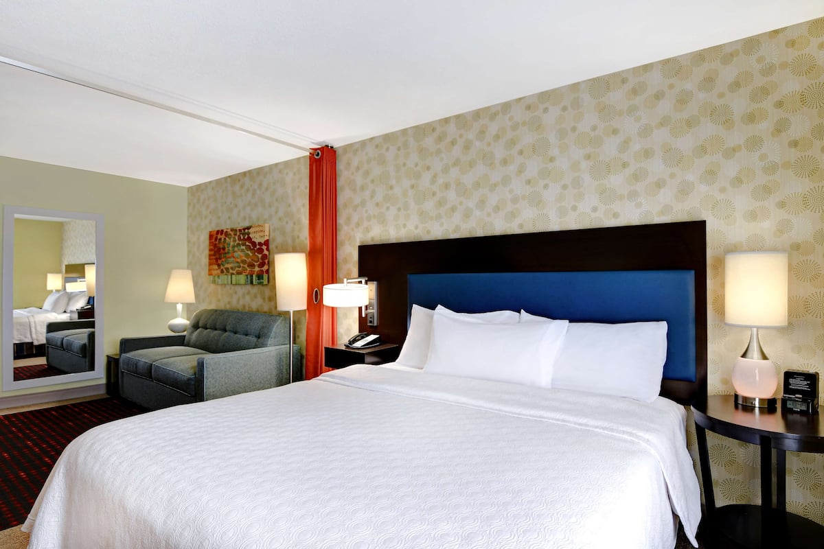 A hotel room with a large bed, two bedside tables, a chair, a mirror, and a patterned wall.