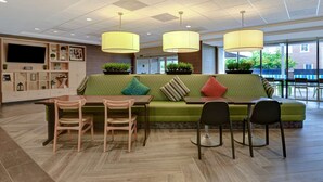 Ein stilvoller Lounge-Bereich mit einem grünen Sofa, Holzstühlen, einem Tisch und Pendelleuchten.