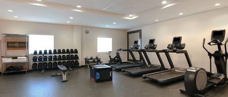 Ett gym med löpband, crosstrainers och en vägg full av hantlar.