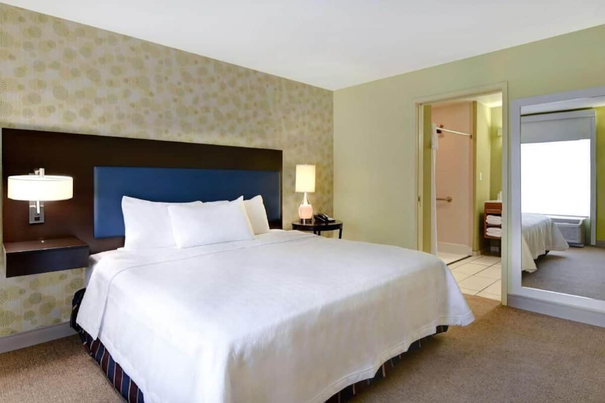 A hotel room with a large bed, bedside lamps, a nightstand, and a door leading to a bathroom.