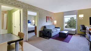Ein Hotelzimmer mit einer Sitzecke, einem kleinen Tisch, einem Sessel, einem Schreibtisch und einem Fenster mit Blick.