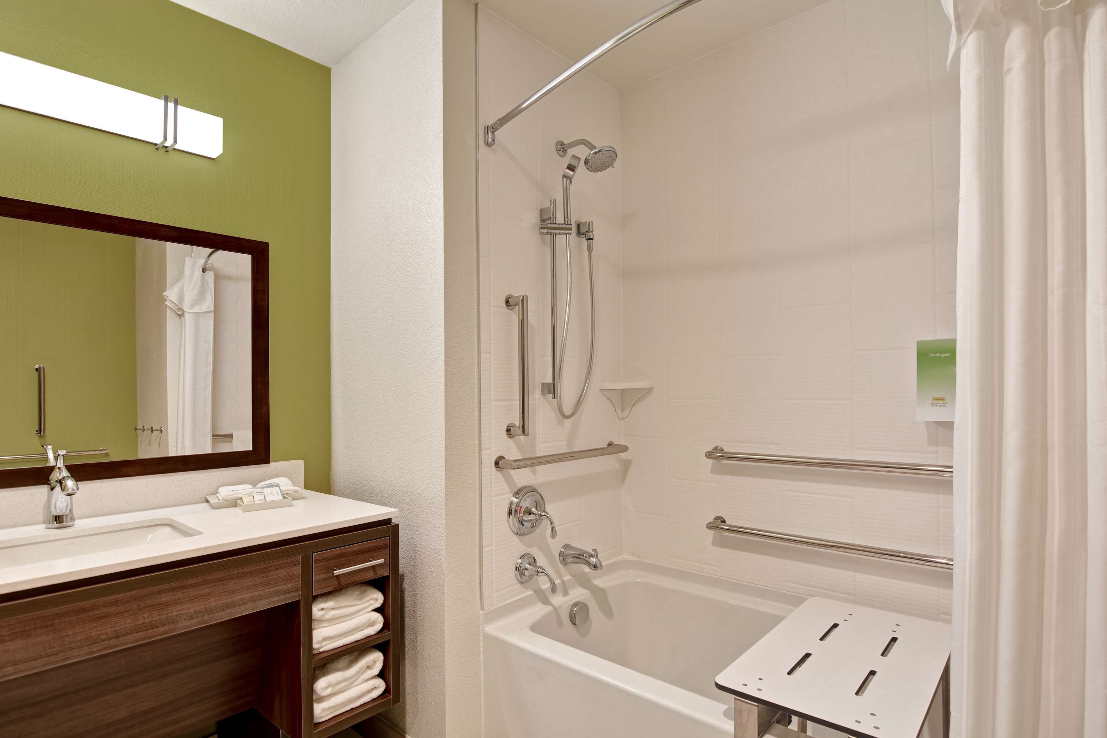 A modern bathroom with a white bathtub, a shower with a handheld showerhead, a vanity with a mirror, and a towel rack.