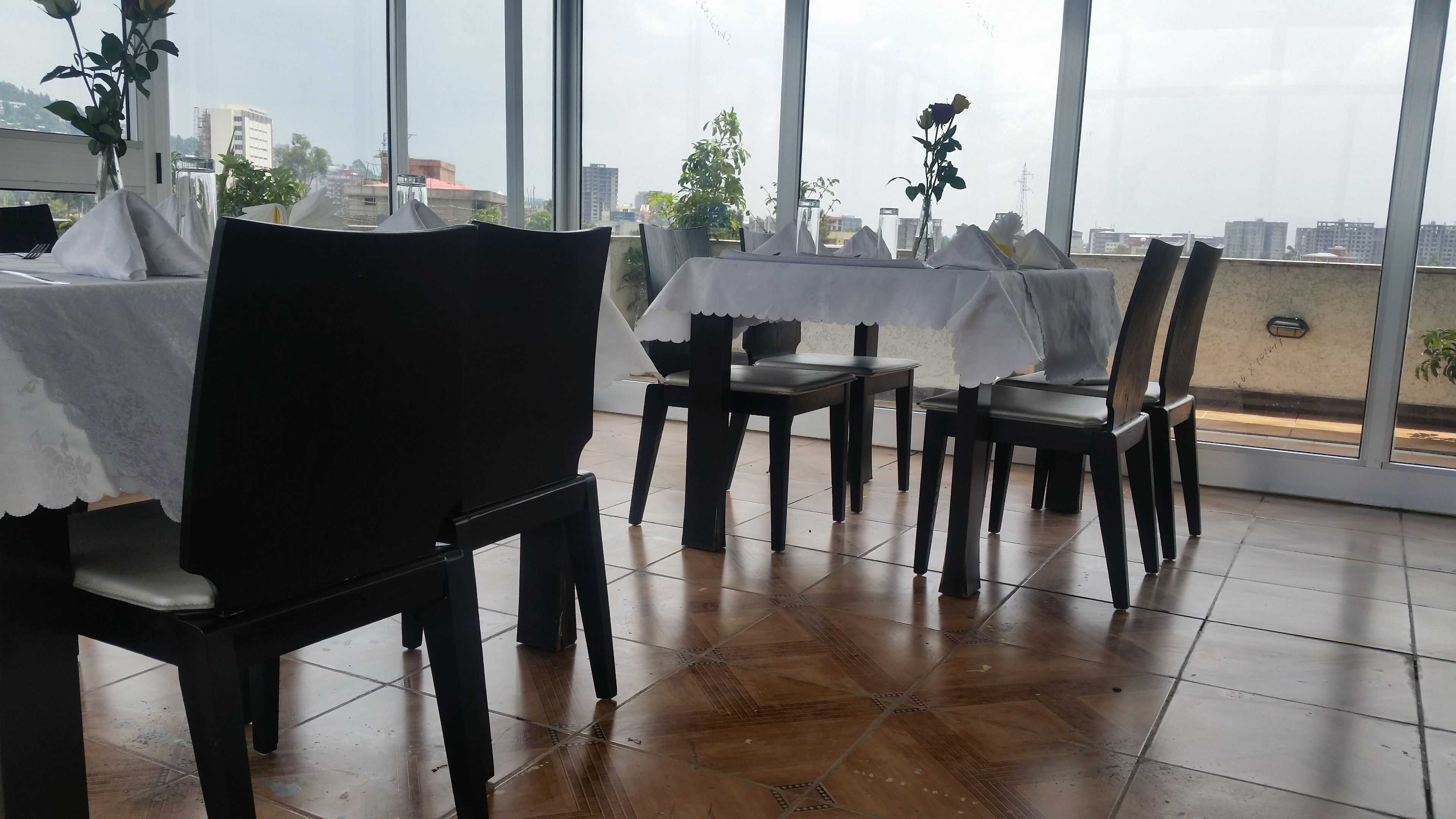 Een eetruimte met tafels bedekt met witte tafelkleden, stoelen en potplanten.