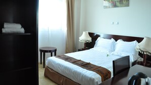 A hotel room with a bed, bedside lamps, a small table, and a painting on the wall. - Ag Palace Hotel (Addis Ababa)