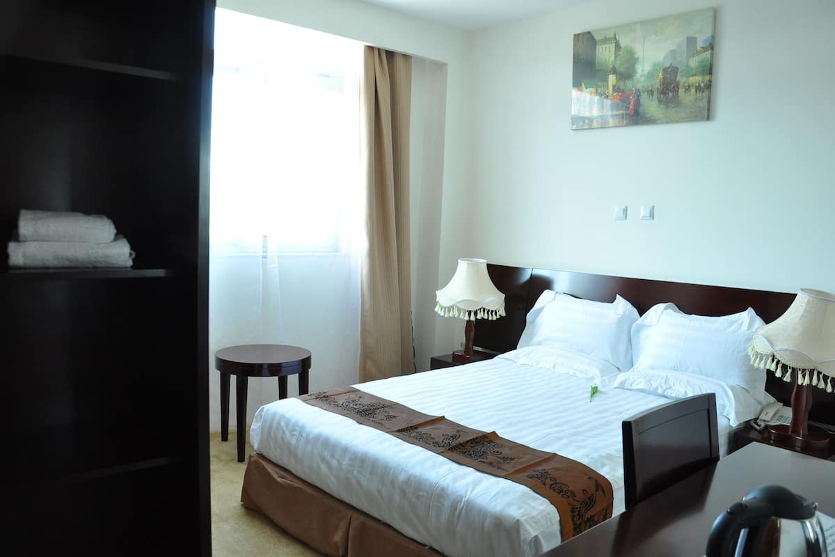 A hotel room with a bed, bedside lamps, a small table, and a painting on the wall.