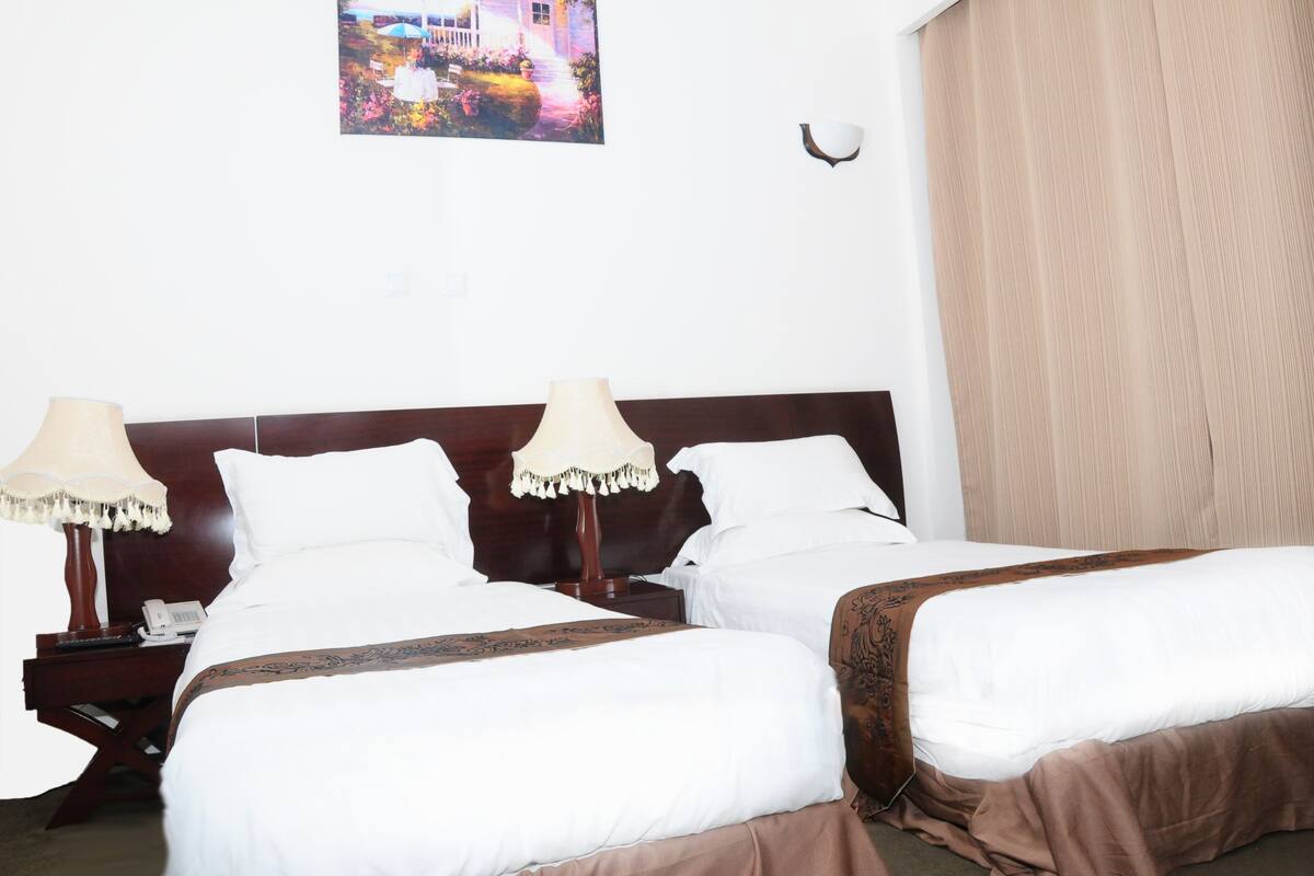 A hotel room with two beds, a nightstand with a lamp, and a painting on the wall.