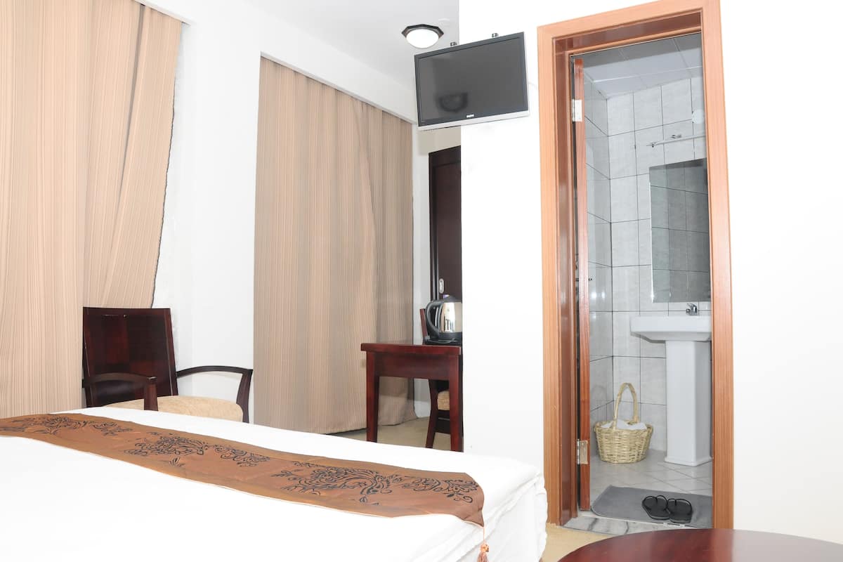 A hotel room with a bed, a desk, a chair, a television, a bathroom with a sink and a mirror, and a door leading to the bathroom.