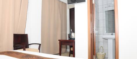 A hotel room with a bed, a desk, a chair, a television, a bathroom with a sink and a mirror, and a door leading to the bathroom.
