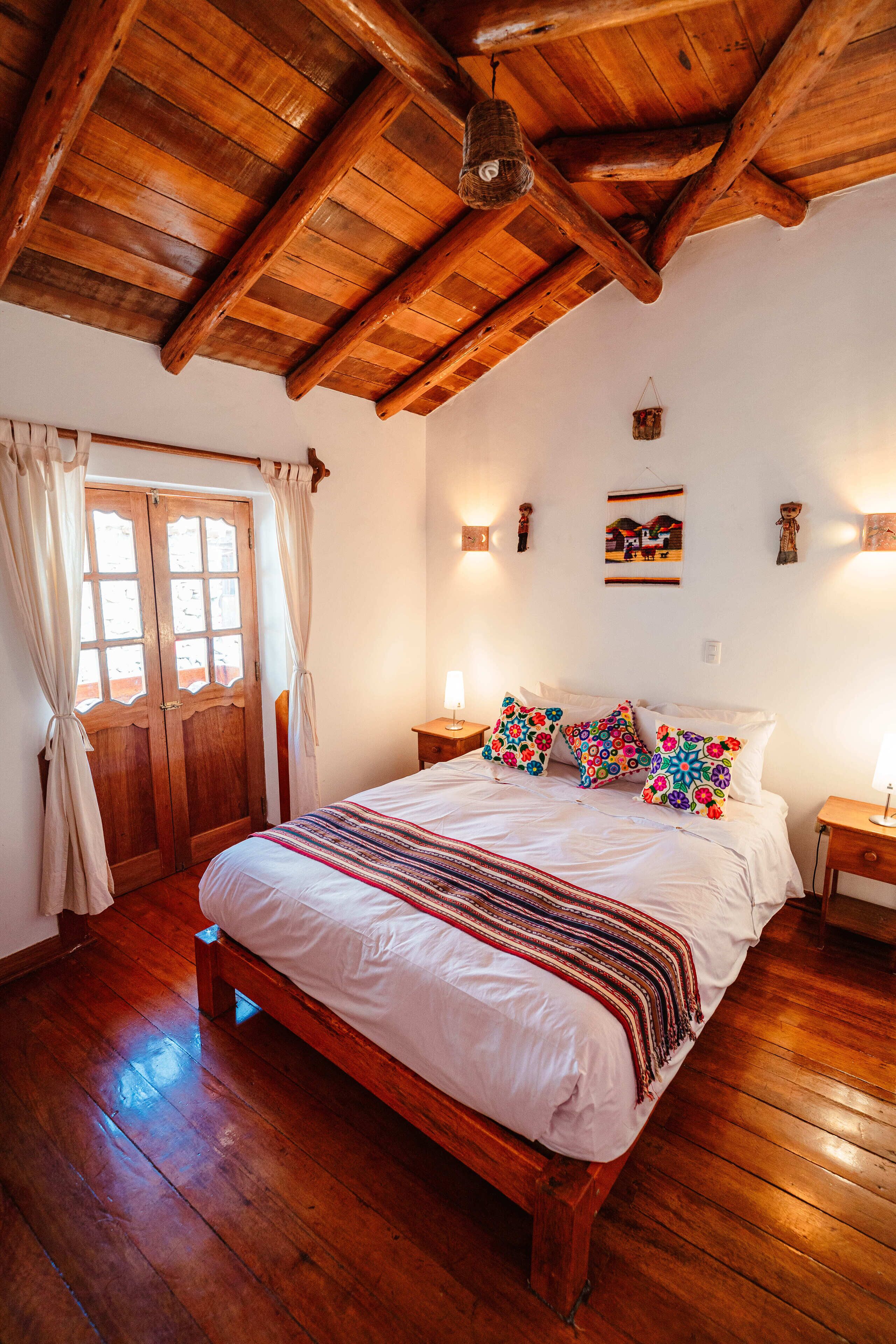 Een slaapkamer met houten frame, een groot bed, houten vloeren en een plafond met zichtbare balken.