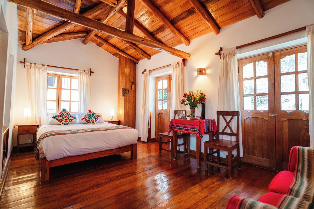 A wooden-framed room with a bed, a table with a red tablecloth, and a chair.