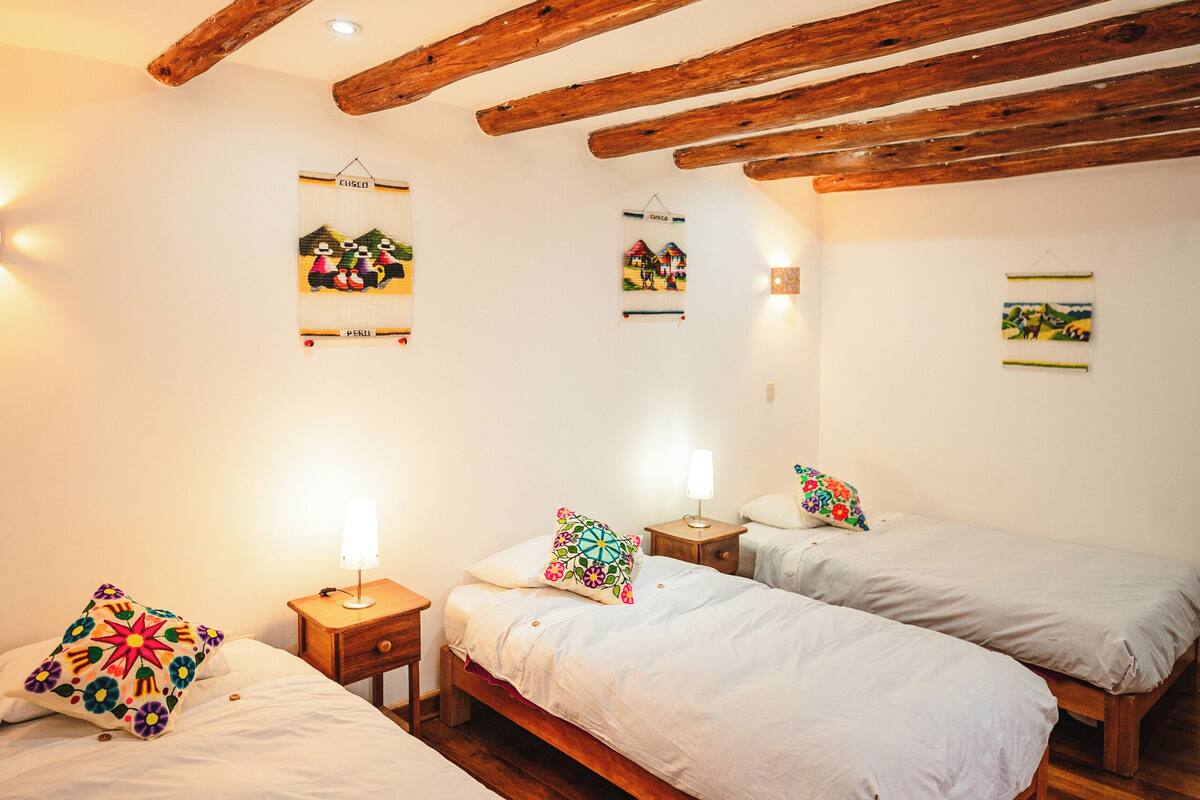 A room with three beds, wooden beams on the ceiling, and wall-mounted artwork.