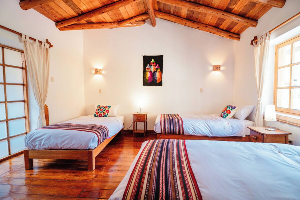 A room with two beds, wooden flooring, a wooden ceiling, and a wall-mounted light fixture.
