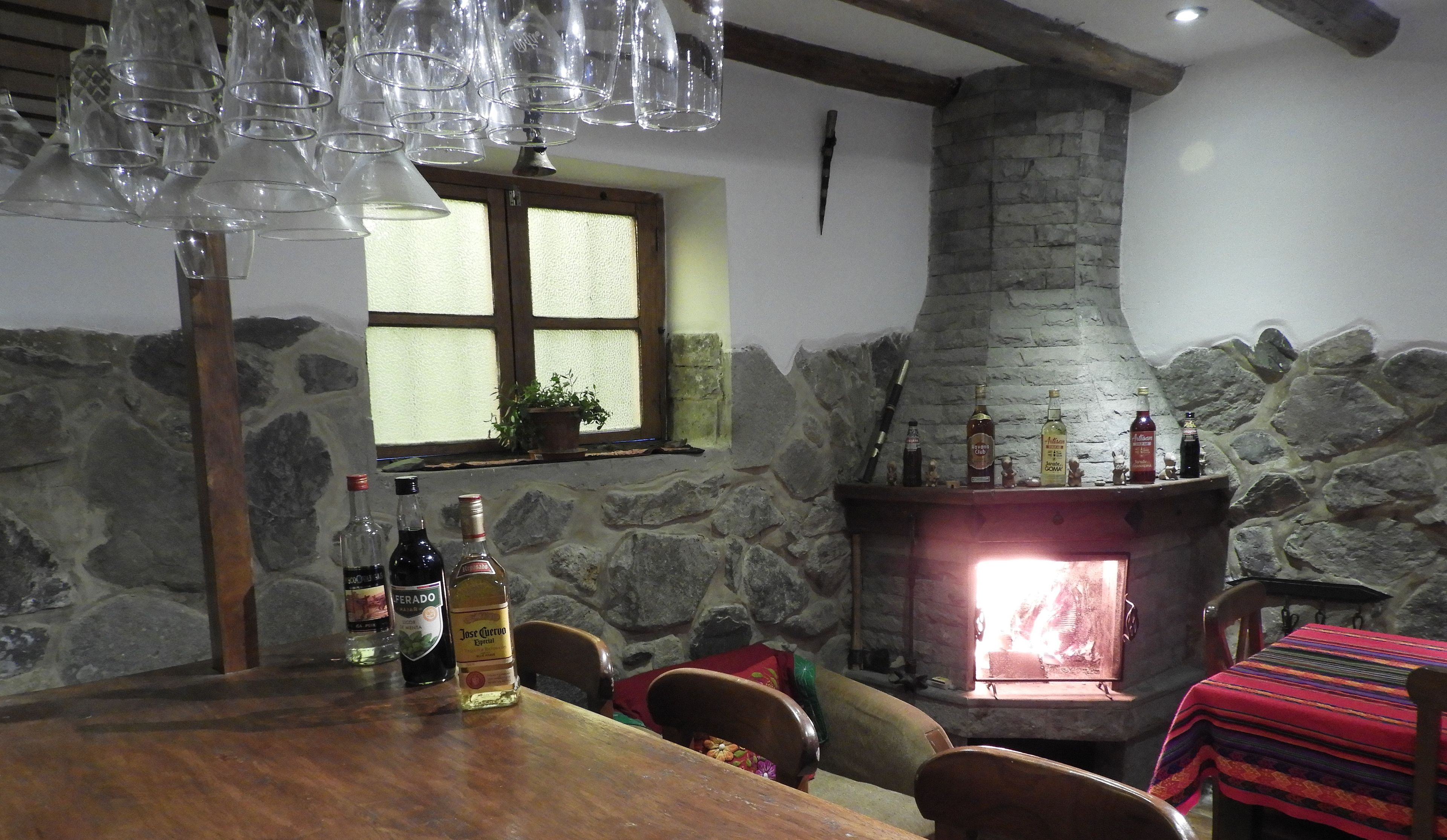 Un interior rústico con chimenea de piedra, vigas de madera y una mesa de comedor con sillas.