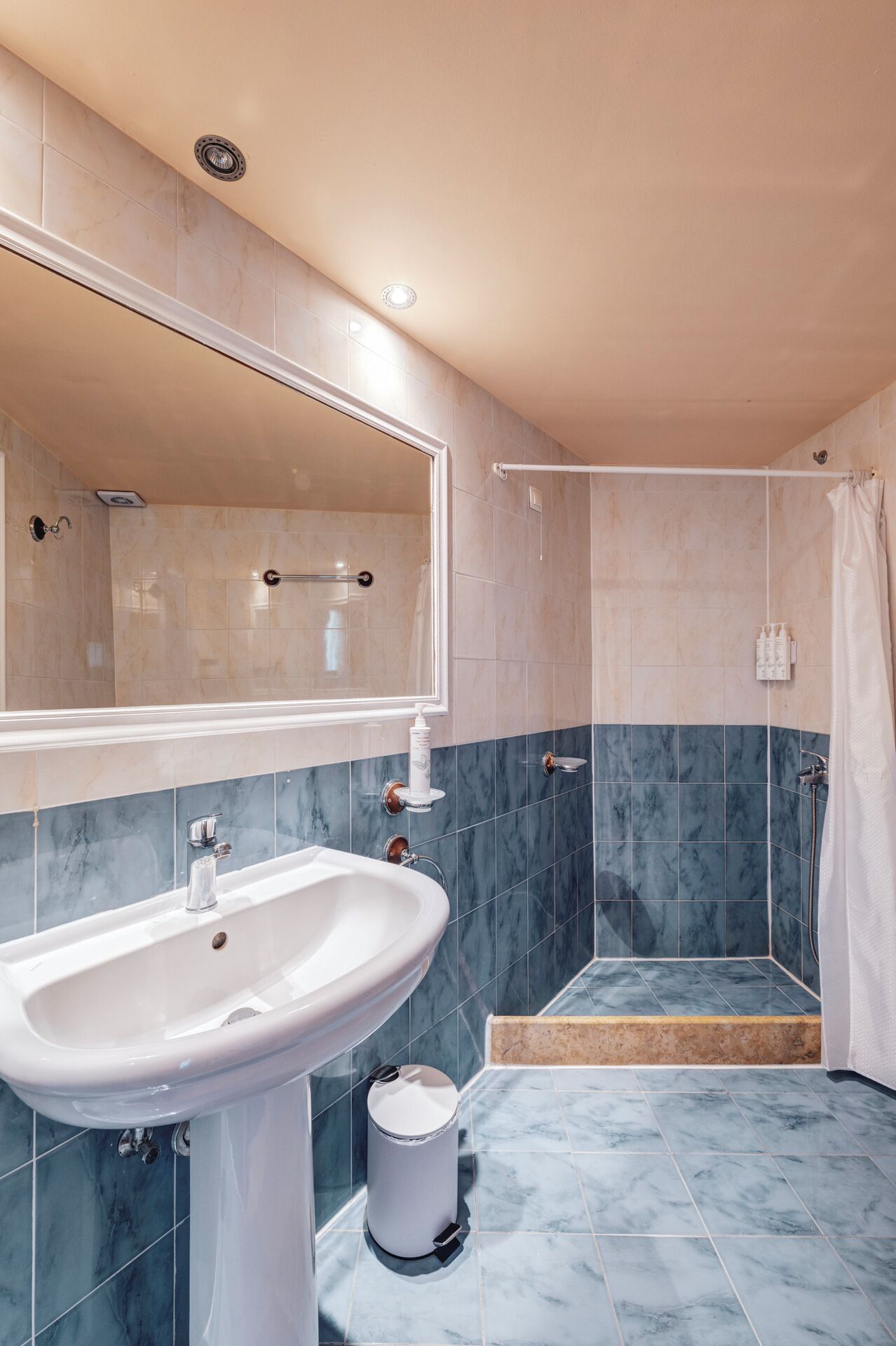 A bathroom with a sink, mirror, shower, and tiled walls.