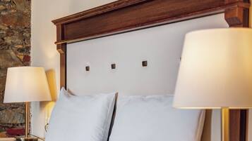 Una cama bien hecha con sábanas blancas, cabecera de madera, dos lámparas de noche y una mesita de noche con lámpara.