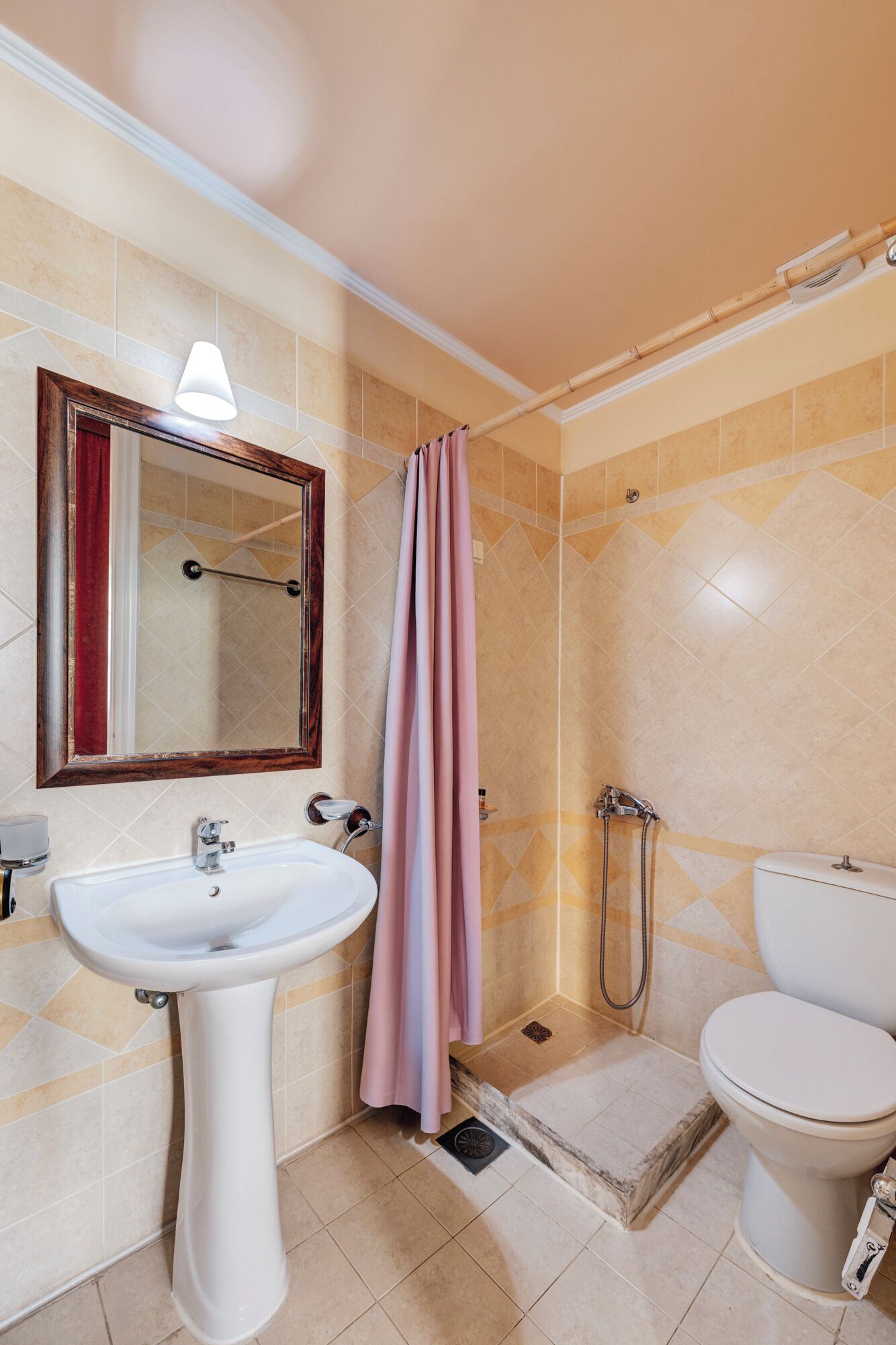 A bathroom with a sink, toilet, shower, and a mirror with a red curtain.
