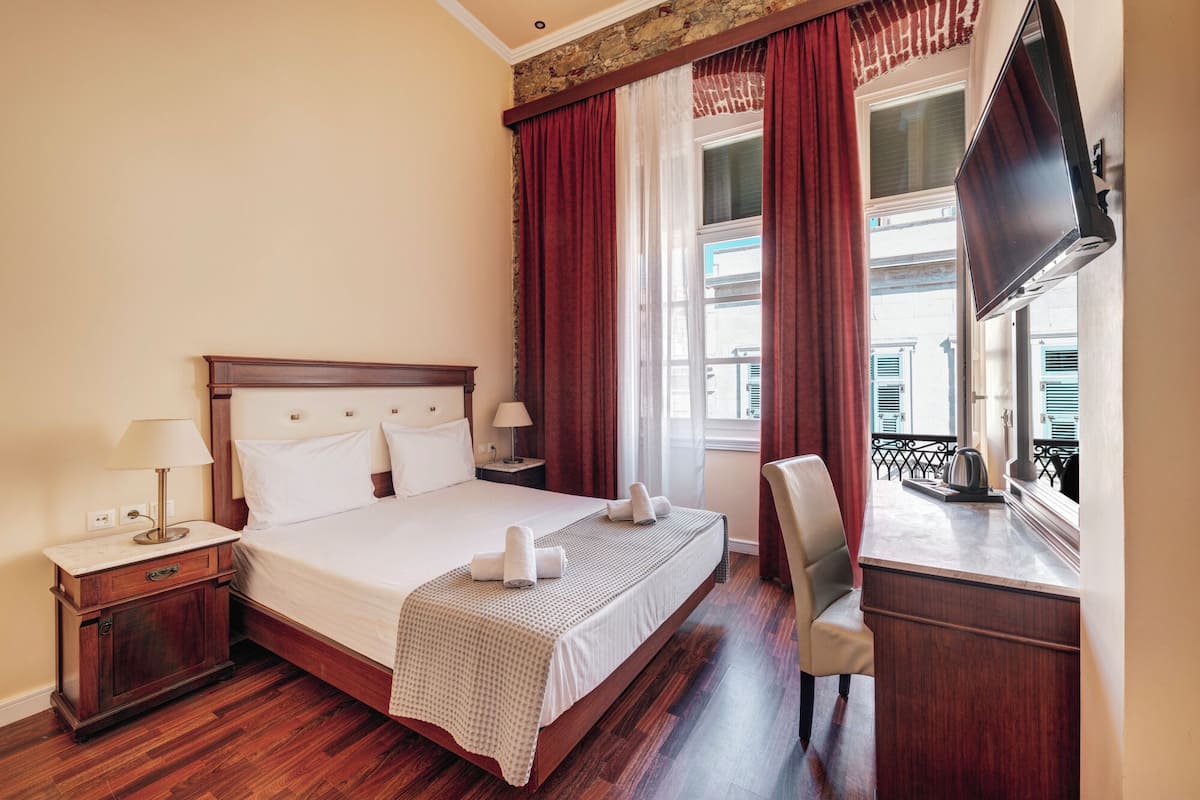 A hotel room with a bed, two bedside tables, a desk, a chair, and a TV.
