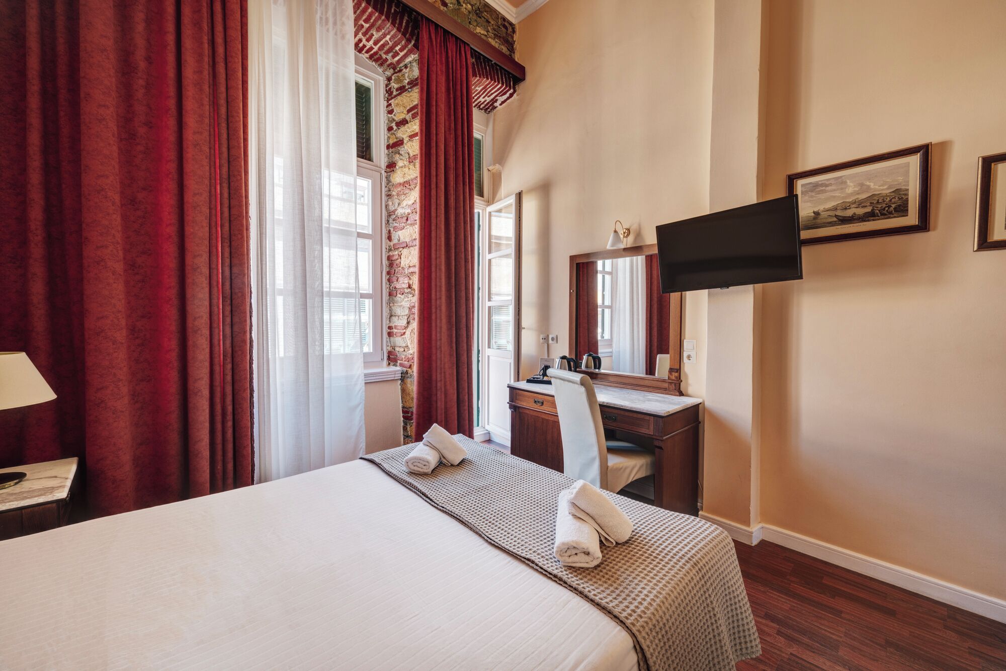 Habitación de hotel con cama, escritorio, espejo, televisor y ventana con cortinas.
