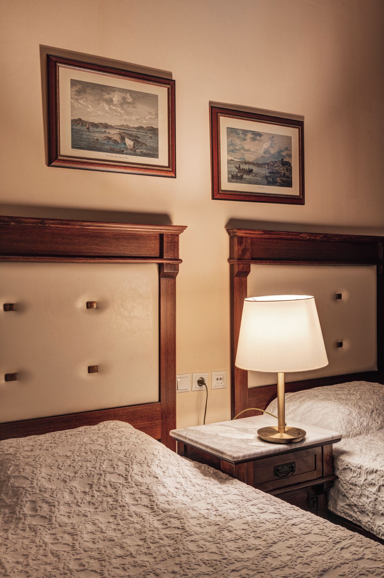 Une chambre d’hôtel avec deux lits, une table de chevet avec une lampe et deux tableaux encadrés au mur.