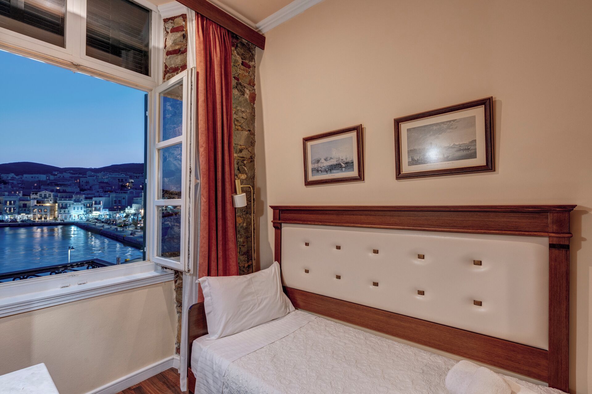 Een hotelkamer met een bed, een raam met uitzicht op een stadsgezicht en twee ingelijste foto's aan de muur.