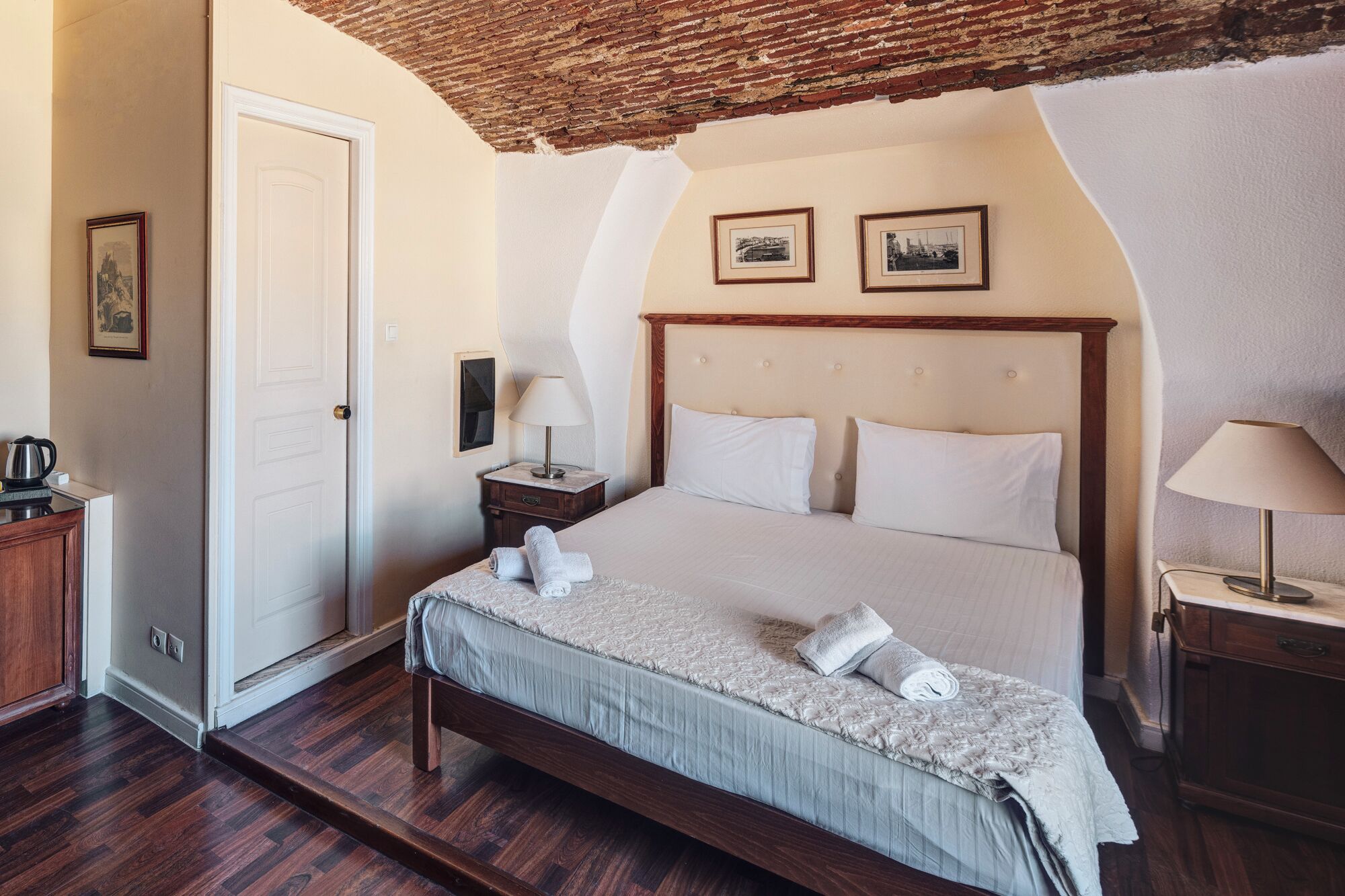 Una habitación de hotel con cama, mesita de noche, lámpara, puerta y un cuadro en la pared.
