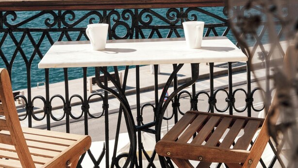 Une vue sur la mer, avec une table et des chaises sur un balcon, donnant sur une ville côtière, avec des bâtiments et une colline en arrière-plan.