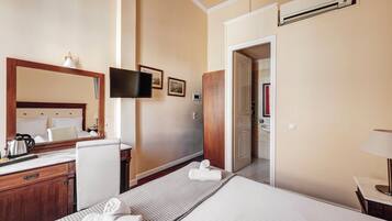 Habitación de hotel con cama, escritorio con hervidor, televisión y baño visible a través de una puerta abierta.