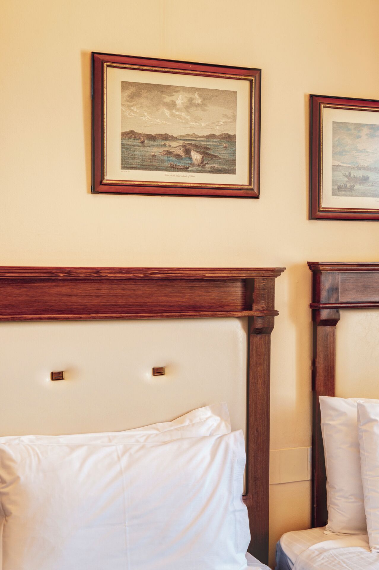 A hotel room with a wooden headboard, two framed landscape paintings, and white bedding.