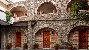 Un edificio de piedra con ventanas y puertas de arco, plantas en macetas y un suelo de piedra con diseño.