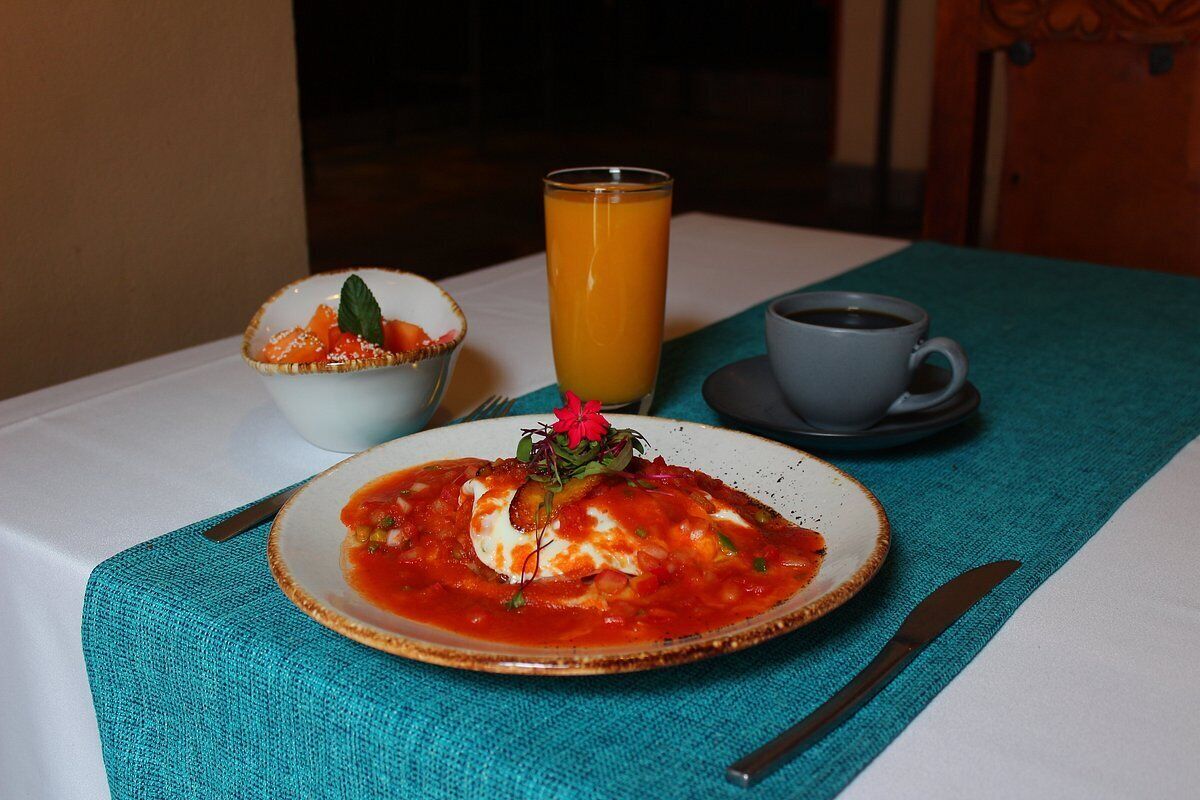 Une table mise pour le petit-déjeuner, avec une assiette de nourriture, un verre de jus d’orange et une tasse de café.