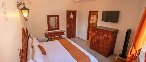 A hotel room with a bed, a desk, a dresser, a mirror, and a television.