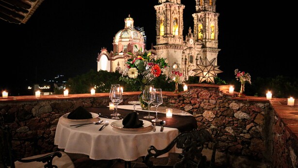 Mesa de comedor para dos personas con velas, un jarrón de flores y vista a un edificio histórico con dos torres.