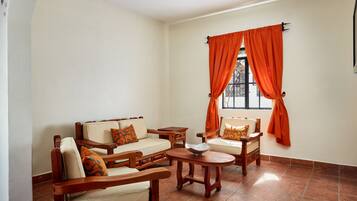 Una sala de estar con un sofá, dos sillones, una mesa de centro y un ventanal con cortinas naranjas.