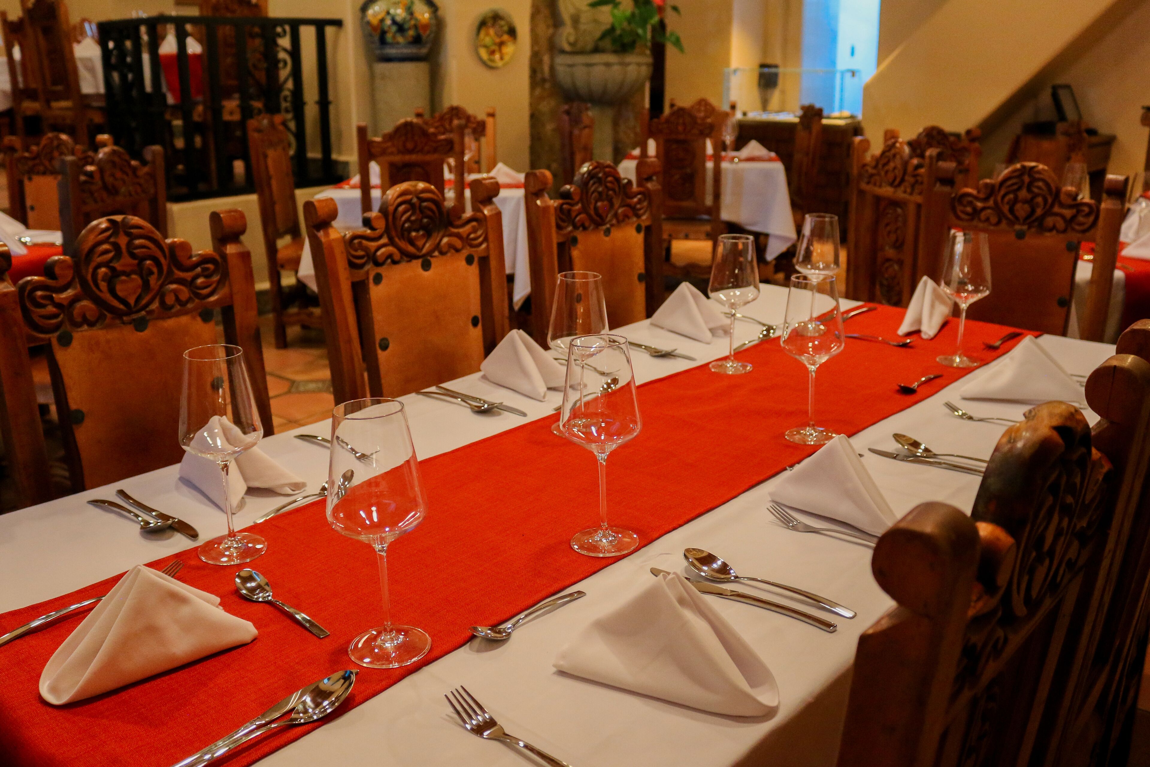 Mesa de jantar posta com toalhas brancas, jogos americanos vermelhos e talheres e copos de vinho organizados.