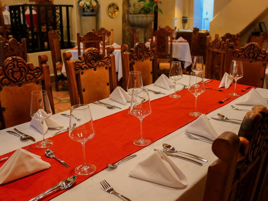 Mesa de jantar posta com toalhas brancas, jogos americanos vermelhos e talheres e copos de vinho organizados.