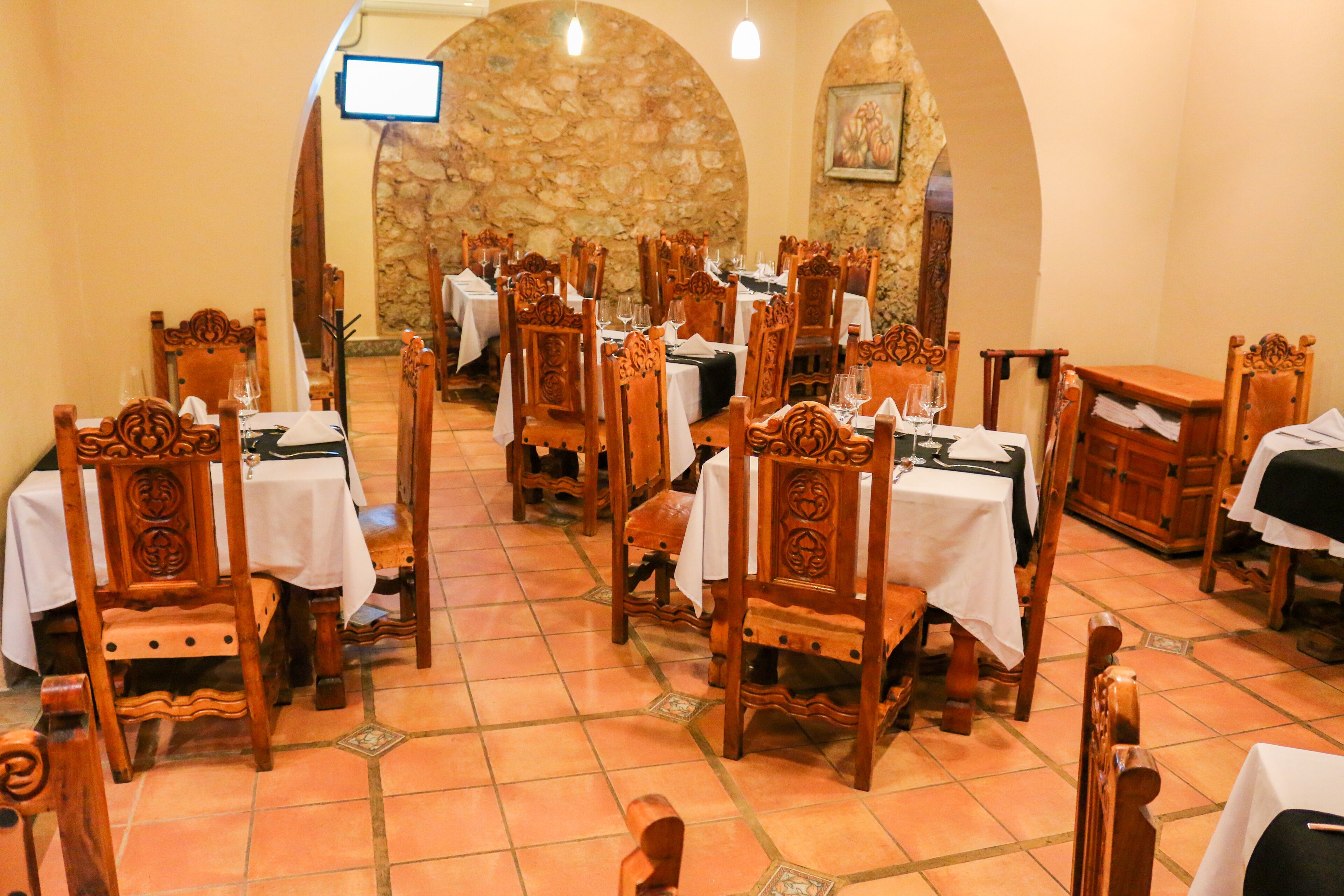 Un restaurant avec des chaises et des tables en bois, des murs en pierre et un sol carrelé.