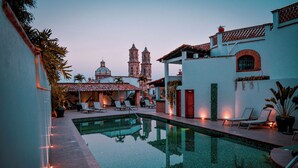 Zona de piscina con sillones de descanso y vista a edificios históricos al fondo.