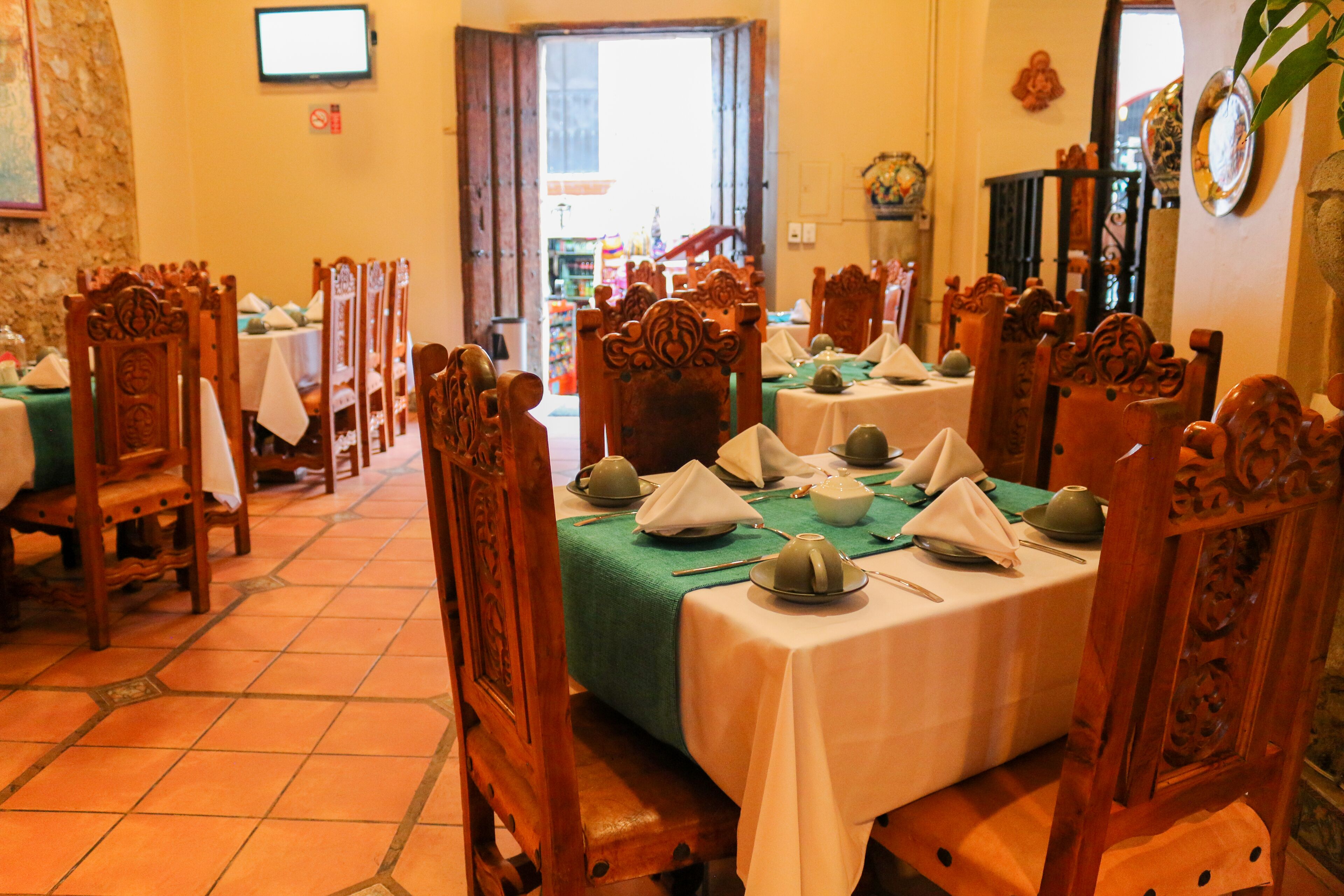 Um restaurante com cadeiras e mesas de madeira, chão de azulejos e uma televisão na parede.