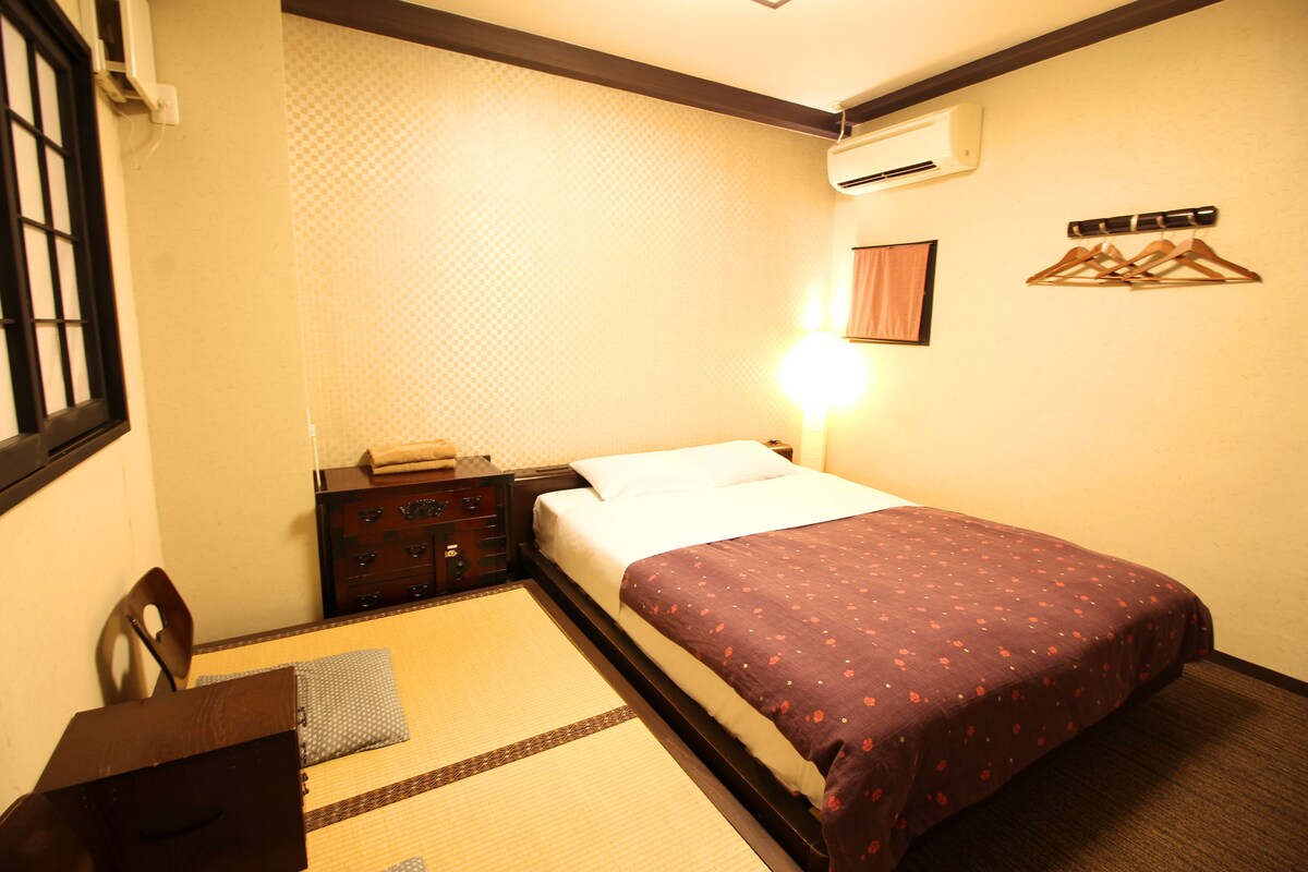 A hotel room with a bed, a bedside table, a dresser, a wall-mounted air conditioner, and a hanging clothes rack.