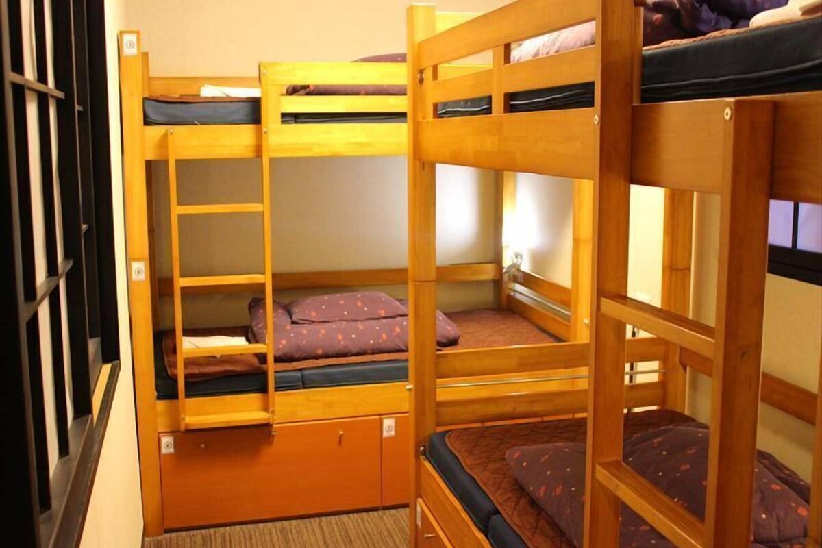 Habitación con literas, suelo de madera, un mueble pequeño y una ventana.
