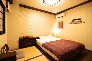 A hotel room with a bed, a bedside table, a chair, a wall-mounted air conditioner, and a wall-mounted light fixture. - K's House Tokyo Oasis - Hostel (Tokyo)