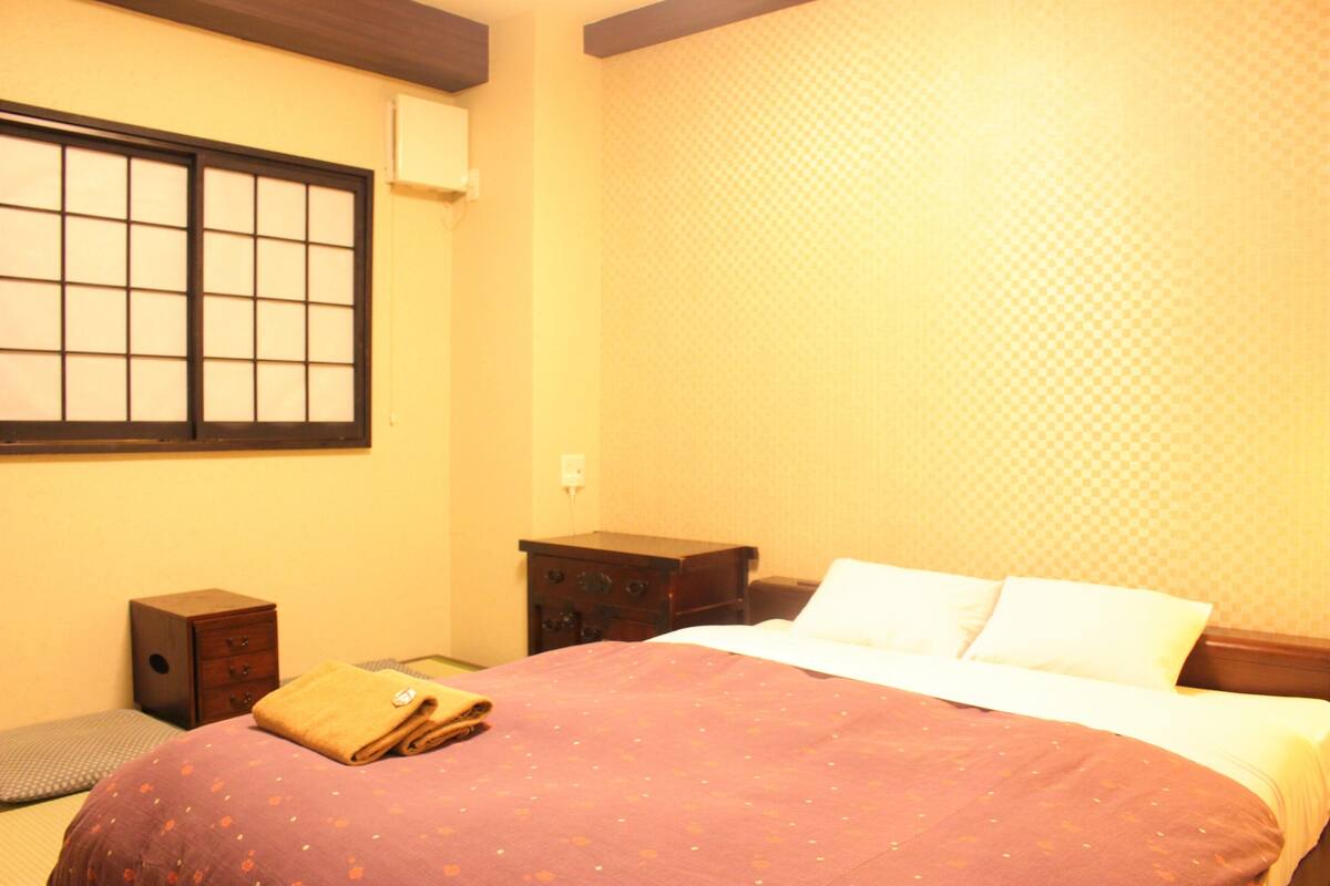 Habitación de hotel con cama, mesita de noche, cómoda y ventana con vistas.