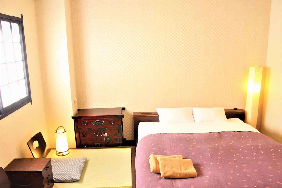 Una habitación de hotel con cama, mesita de noche, lámpara, cómoda y ventana.