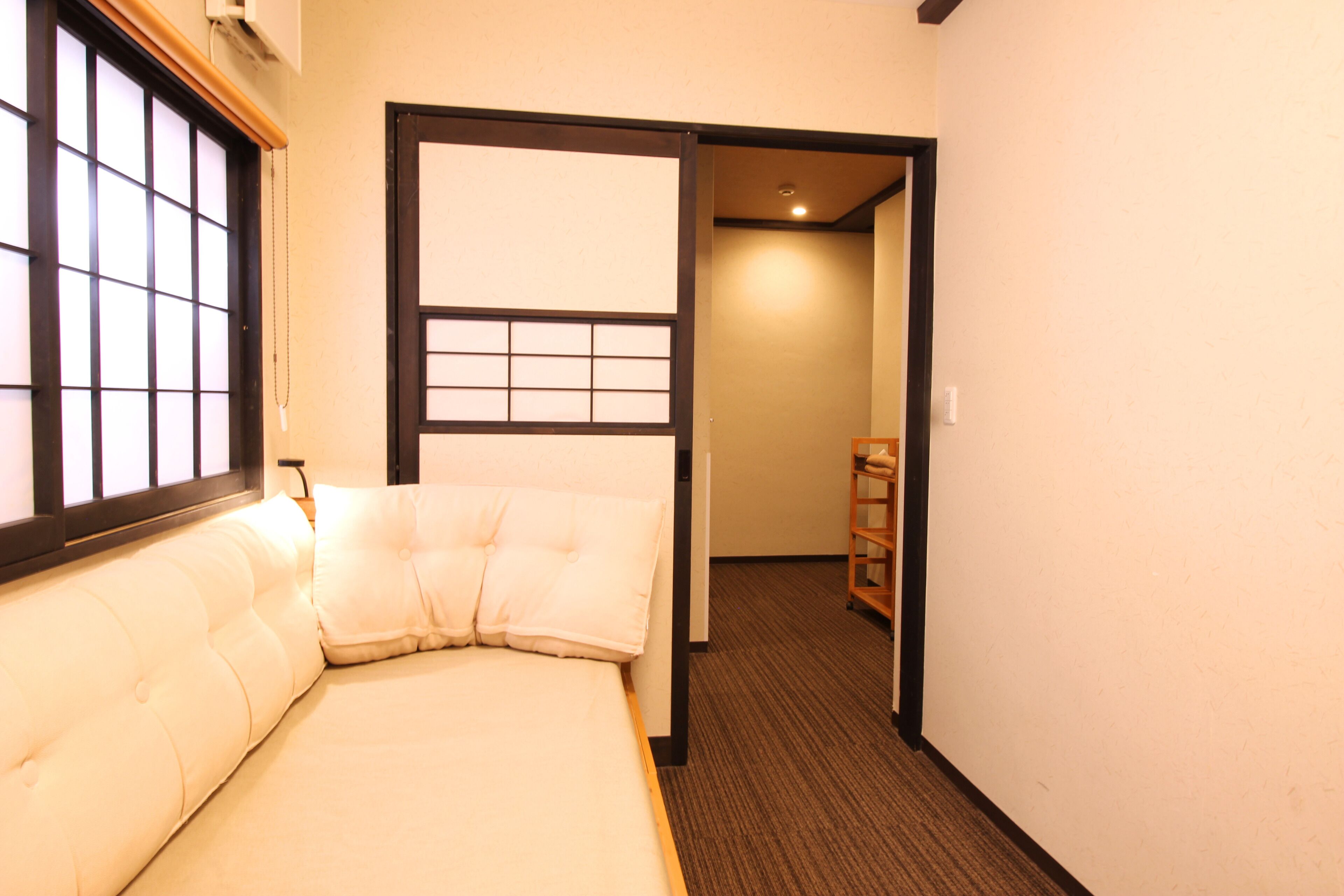 A room with a bed, a window with a grid pattern, and a wooden door leading to another room.