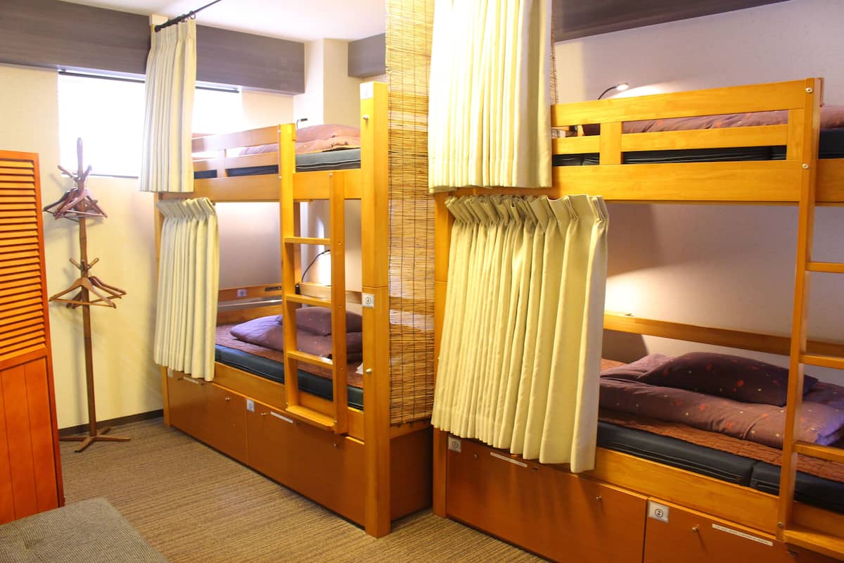 Una habitación con literas, un perchero y un mueble pequeño.