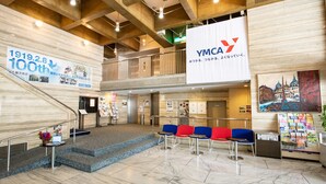 A spacious lobby with a high ceiling, a staircase, and a reception area with a banner. - YMCA Asia Youth Center (Tokyo)