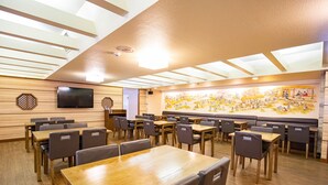 A restaurant with wooden tables and chairs, a large mural on the wall, and a flat-screen TV mounted on the wall. - YMCA Asia Youth Center (Tokyo)